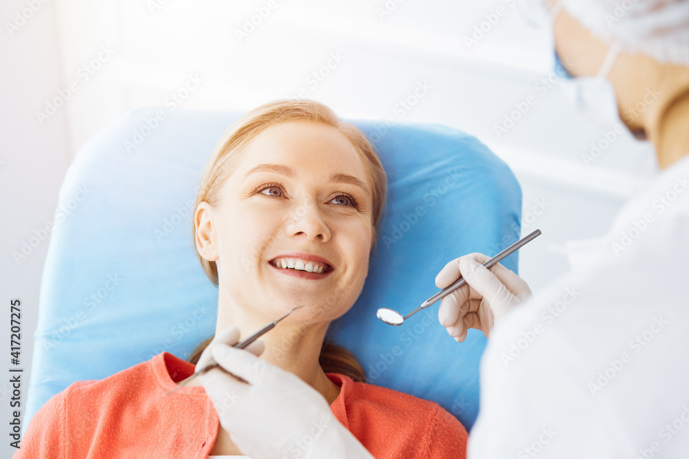 Happy smiling woman is being examined by dentist at dental clinic. Healthy teeth and medicine, stomatology concept Happy smiling woman is being examined by dentist at dental clinic. Healthy teeth and medicine, stomatology concept