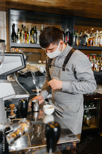 A masked barista prepares delicious coffee at the bar in a cafe. The work of restaurants and cafes during the pandemic.