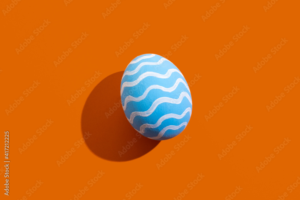 Easter art. Festive ornament. Spring holiday. Handmade decoration. Abstract background. Blue egg with white pattern waves isolated on orange copy space. Easter art. Festive ornament. Spring holiday. Handmade decoration. Abstract background. Blue egg with white pattern waves isolated on orange copy space.