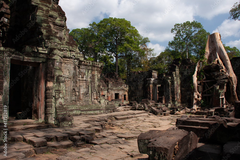 Ancient temples in Angkor covered by old trees in the middle of the jungle with the entrance to one temple in the foreground