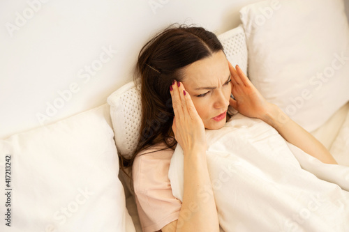 beautiful young woman lies on bed under the covers with a cold 