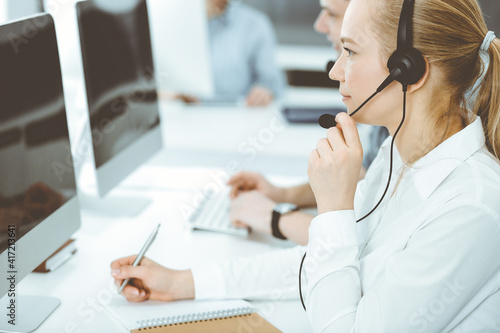 Call center. Group of casual dressed operators at work. Blond business woman in headset at customer service office. Telesales in business