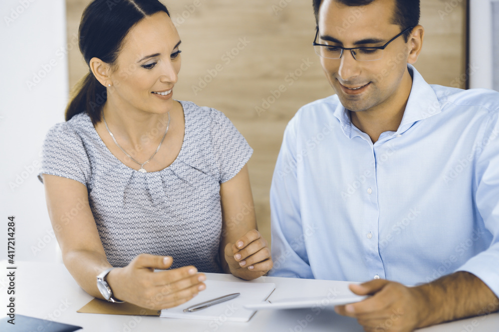 Businessman and hispanic business woman working with computer in a modern office. Group of diverse people. Teamwork, partnership and business concept Businessman and hispanic business woman working with computer in a modern office. Group of diverse people. Teamwork, partnership and business concept