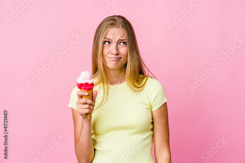 Young russian woman eating an ice cream isolated confused, feels doubtful and unsure.