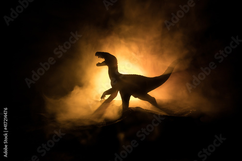 Silhouette of giant Dinosaur in dark foggy night. Creative decoration with little miniature. Burning misty background.