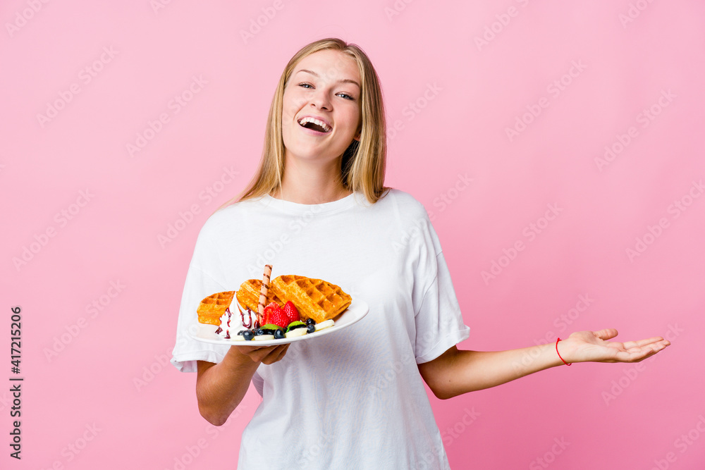 Young russian woman eating a waffle isolated showing a welcome expression.