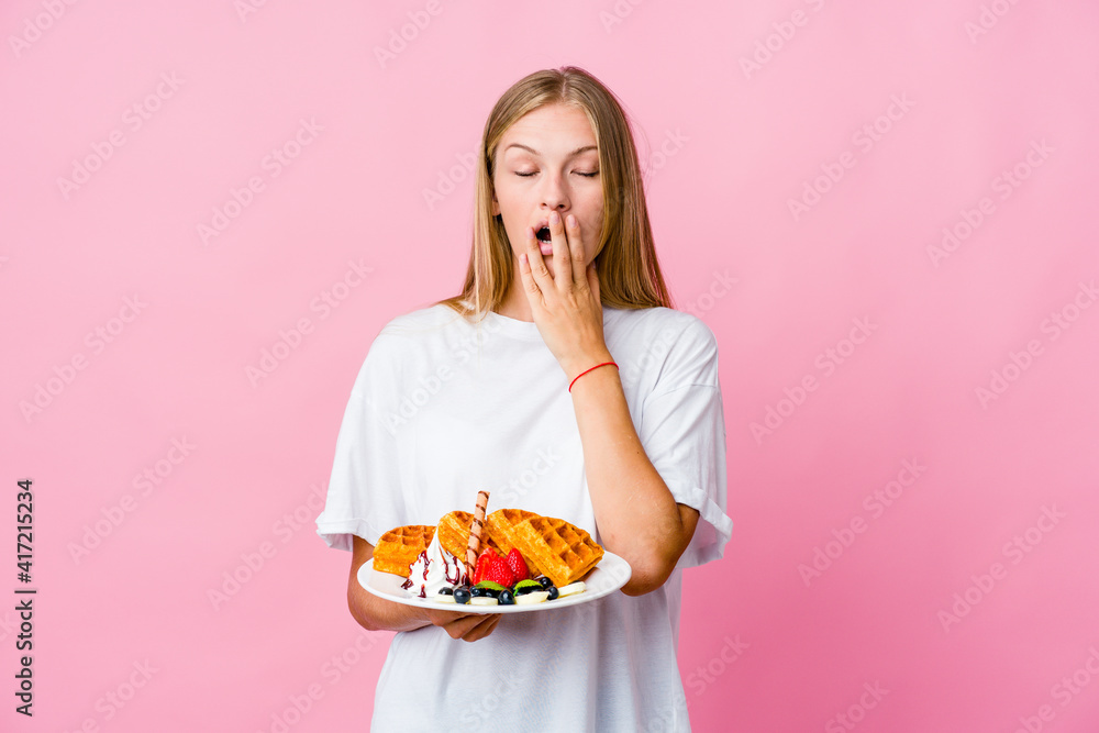 Young russian woman eating a waffle isolated yawning showing a tired gesture covering mouth with hand. Young russian woman eating a waffle isolated yawning showing a tired gesture covering mouth with hand.