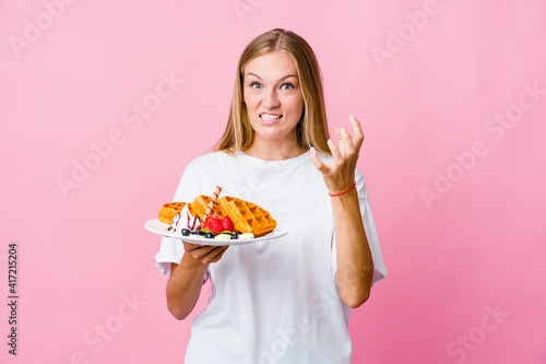 Young russian woman eating a waffle isolated upset screaming with tense hands.