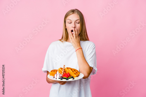 Young russian woman eating a waffle isolated yawning showing a tired gesture covering mouth with hand.