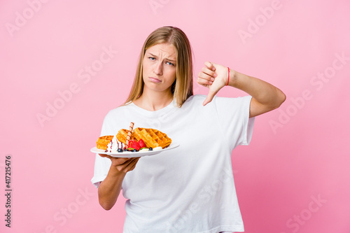 Young russian woman eating a waffle isolated showing thumb down and expressing dislike.