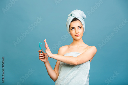 Displeased angry woman against of shaving, holds razor in hand, supports wax depilation, poses half nude, shows bare shoulders, frowns face, isolated over blue background. Women and hygiene concept photo