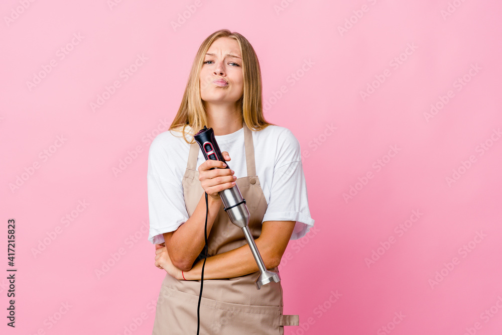 Young russian cook woman holding an electric mixer isolated frowning face in displeasure, keeps arms folded. Young russian cook woman holding an electric mixer isolated frowning face in displeasure, keeps arms folded.