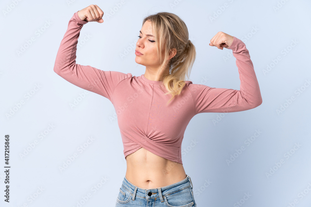 Blonde woman over isolated blue background doing strong gesture Blonde woman over isolated blue background doing strong gesture