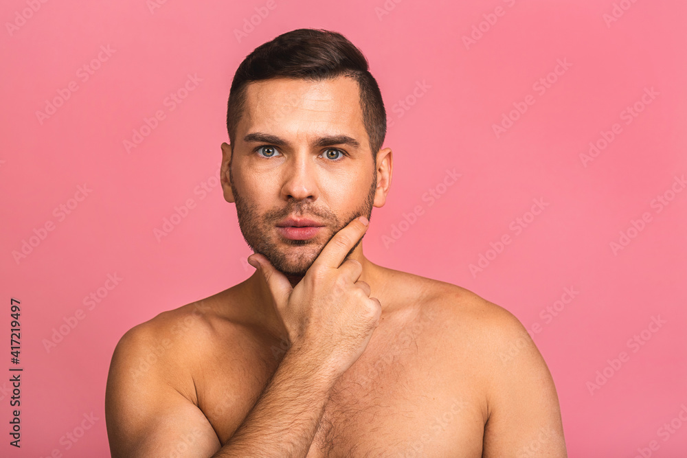 Fototapeta premium Photo of smiling young beautiful man standing isolated over pink wall background naked. Man's skincare concept in a bathroom.