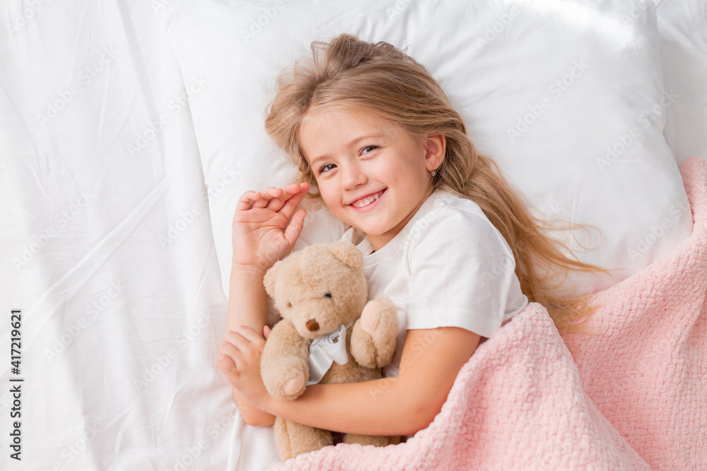 little blonde girl sleeping in bed hugging a teddy bear under a pink knitted blanket, space for text little blonde girl sleeping in bed hugging a teddy bear under a pink knitted blanket, space for text