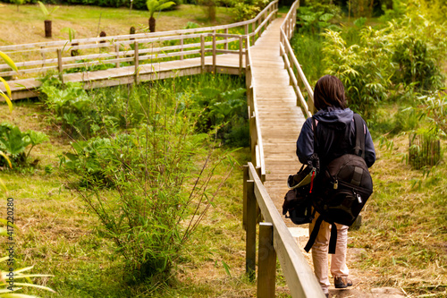 Fotografie a young adventurer woman walking alone on a narrow wooden hiking path carrying big bags