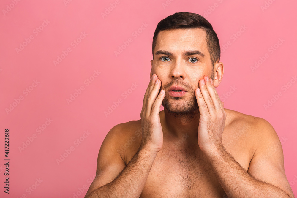 Obraz premium Photo of smiling young beautiful man standing isolated over pink wall background naked. Man's skincare concept in a bathroom.