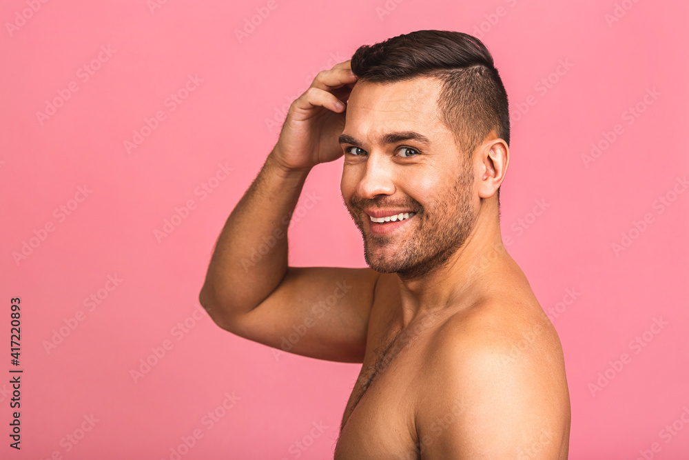 Photo of smiling young beautiful man standing isolated over pink wall background naked. Man's skincare concept in a bathroom. Photo of smiling young beautiful man standing isolated over pink wall background naked. Man's skincare concept in a bathroom.