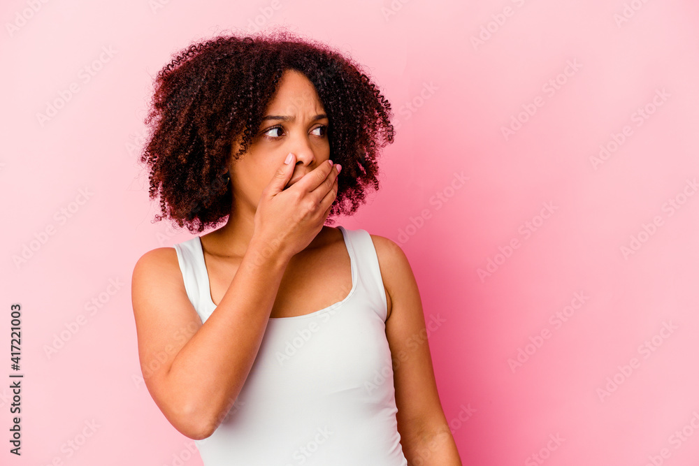 Young african american mixed race woman isolated thoughtful looking to a copy space covering mouth with hand.