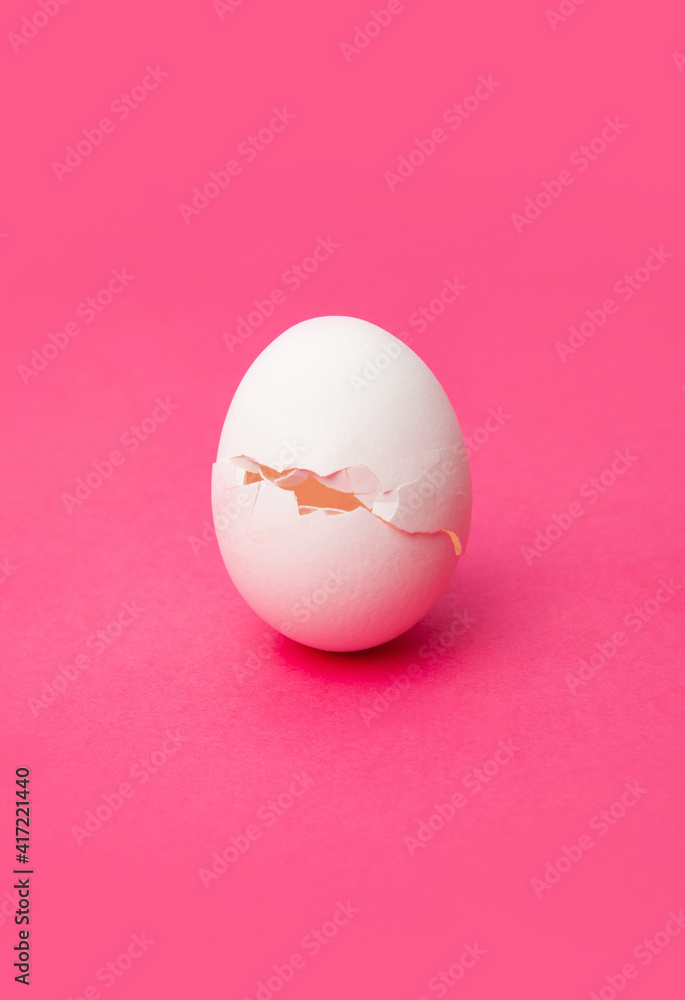 Cracked fresh white egg on pink table
