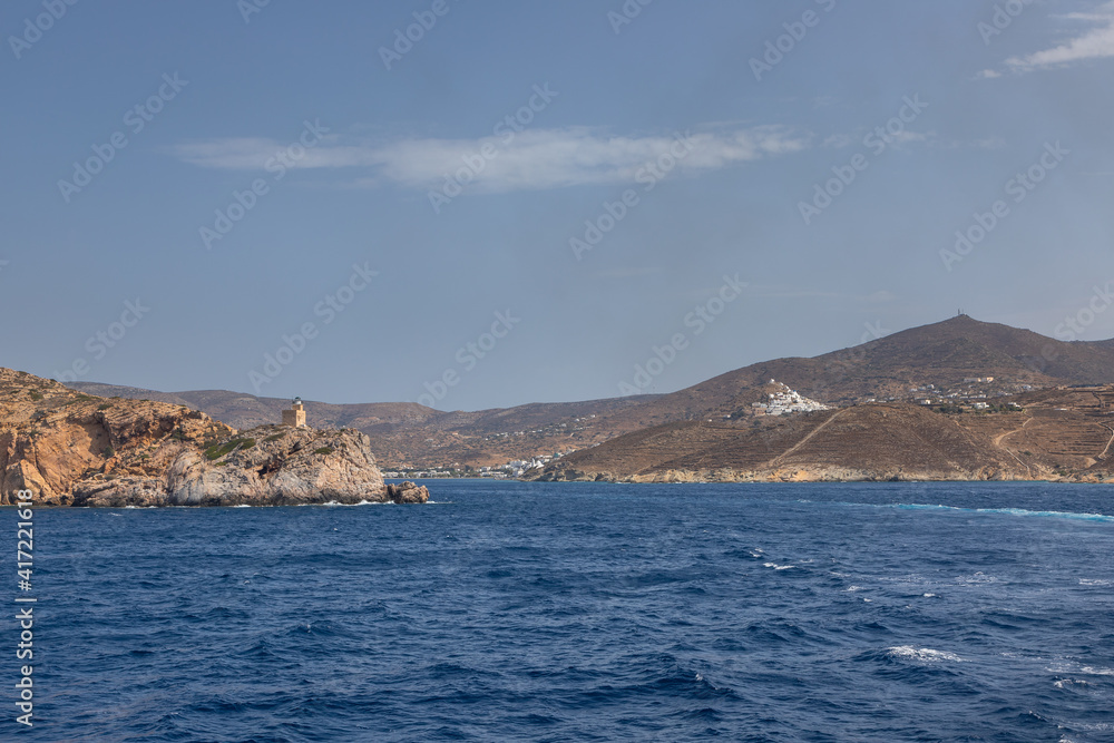 Lighthouse on the rock in the background. Chora , Ios Island, Greece.