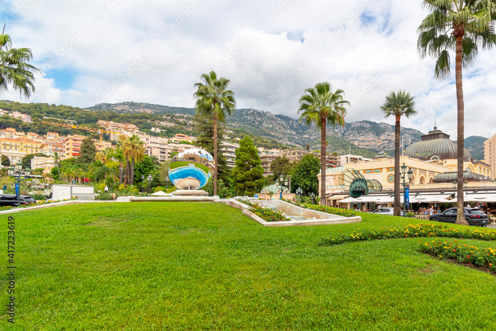 The famous casino is reflected in the large round mirror in the casino gardens with the city and mountains behind in the coastal resort city of Monte Carlo, Monaco.