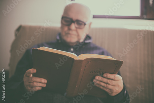 Elderly man sitting on couch and reading Bible