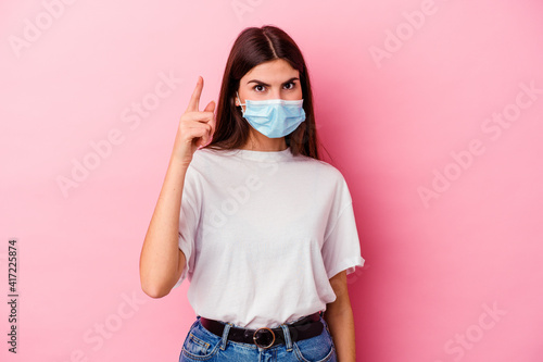 Young caucasian woman wearing a mask for virus isolated on pink background having an idea  inspiration concept.