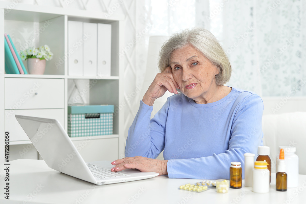 ill beautiful senior woman with pills using laptop ill beautiful senior woman with pills using laptop
