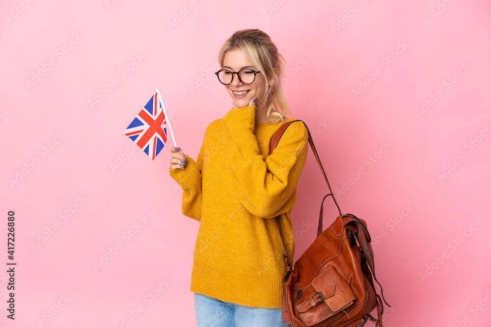 Young Russian woman holding an United Kingdom flag isolated on pink background looking to the side and smiling Young Russian woman holding an United Kingdom flag isolated on pink background looking to the side and smiling