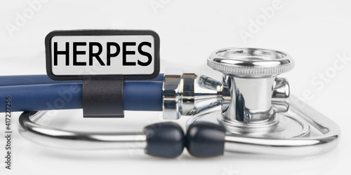 On the white surface lies a stethoscope with a plate with the inscription - HERPES