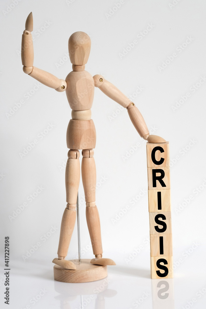 The wooden man raised his hand, and under his left hand he has cubes with the inscription -CRISIS The wooden man raised his hand, and under his left hand he has cubes with the inscription -CRISIS