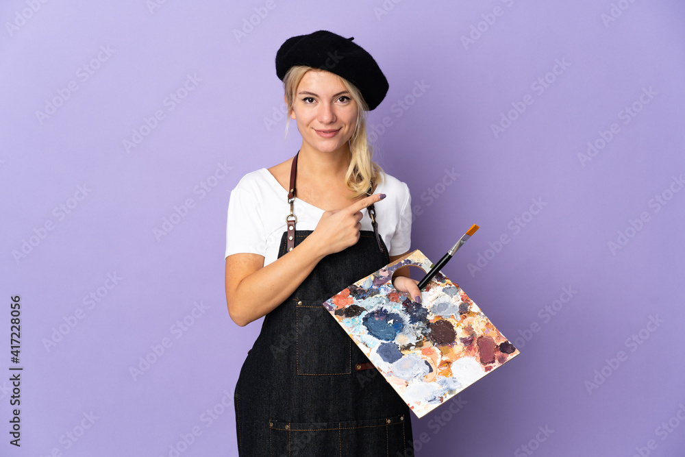 Young artist Russian woman holding a palette isolated on purple background pointing to the side to present a product Young artist Russian woman holding a palette isolated on purple background pointing to the side to present a product