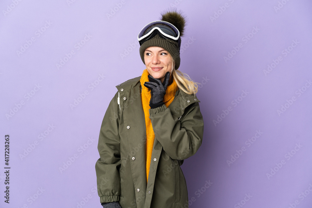 Skier Russian girl with snowboarding glasses isolated on purple background thinking an idea while looking up Skier Russian girl with snowboarding glasses isolated on purple background thinking an idea while looking up