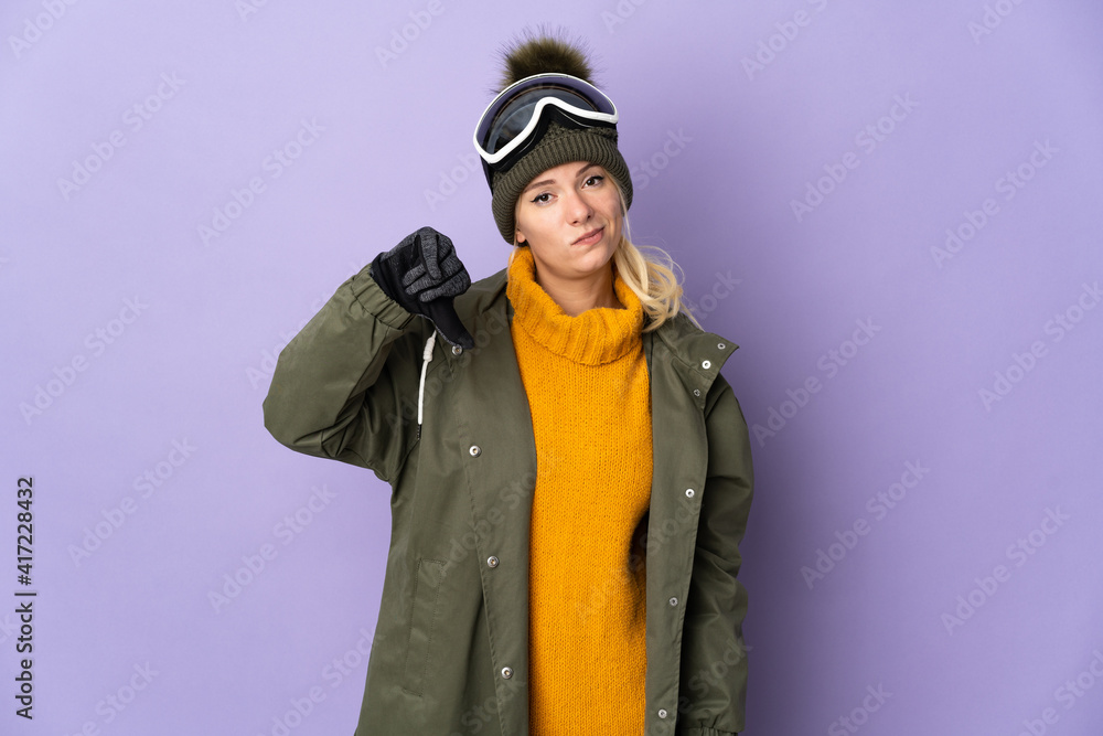 Skier Russian girl with snowboarding glasses isolated on purple background showing thumb down with negative expression Skier Russian girl with snowboarding glasses isolated on purple background showing thumb down with negative expression