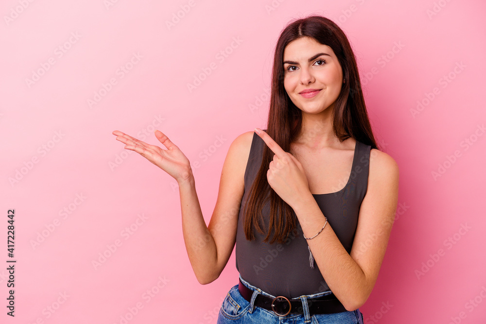 Young caucasian woman isolated on pink background excited holding a copy space on palm. Young caucasian woman isolated on pink background excited holding a copy space on palm.