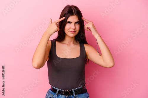 Young caucasian woman isolated on pink background focused on a task, keeping forefingers pointing head. © Asier