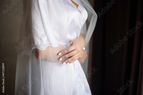 The bride in a dressing gown hugs herself.