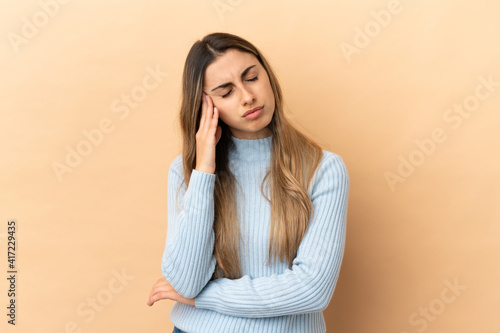 Young caucasian woman isolated on beige background with headache