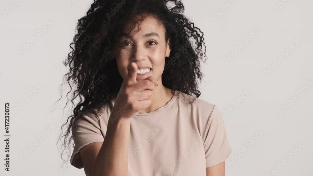 Young cheerful dark fluffy haired Afro woman indicate straightly at camera with index finger and smiling over white background. Yes, I choose you expression Young cheerful dark fluffy haired Afro woman indicate straightly at camera with index finger and smiling over white background. Yes, I choose you expression
