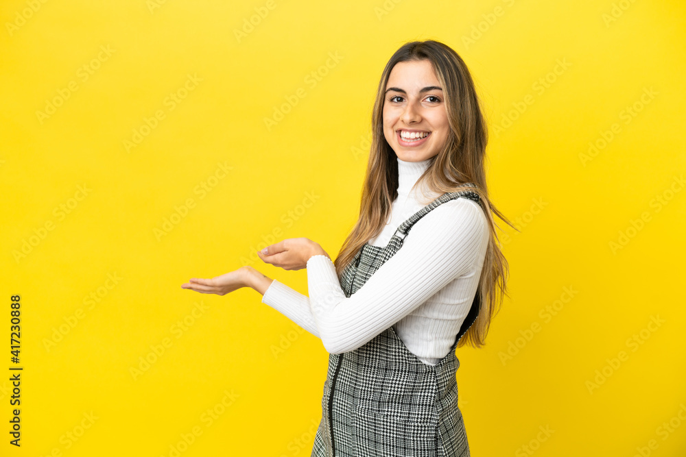 Young caucasian woman isolated on yellow background extending hands to the side for inviting to come Young caucasian woman isolated on yellow background extending hands to the side for inviting to come