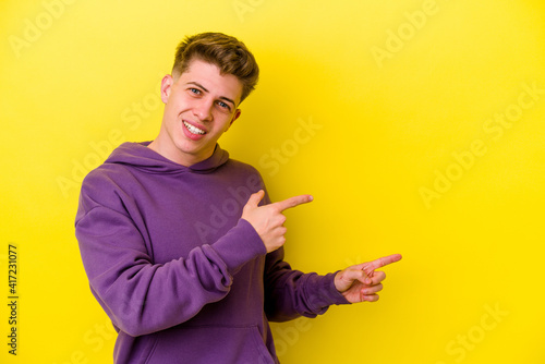 Young caucasian man isolated on yellow background excited pointing with forefingers away.