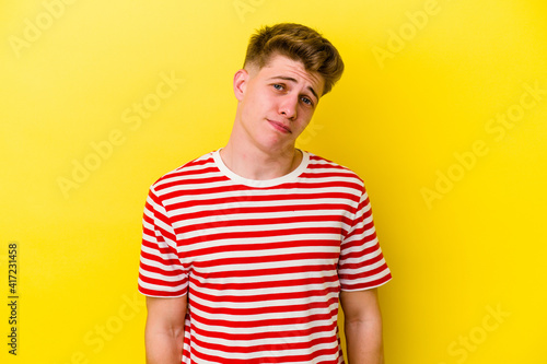 Young caucasian man isolated on yellow background shrugs shoulders and open eyes confused.