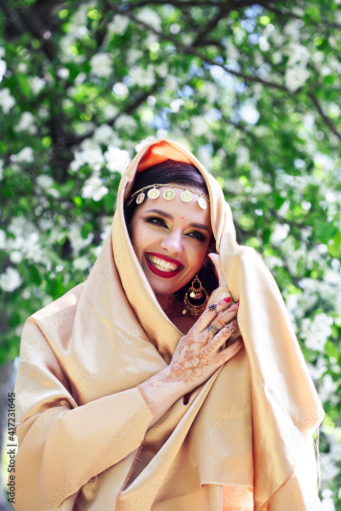 young pretty indian girl in jewelry and veil posing cheerful happy smiling in green park, lifestyle people concept