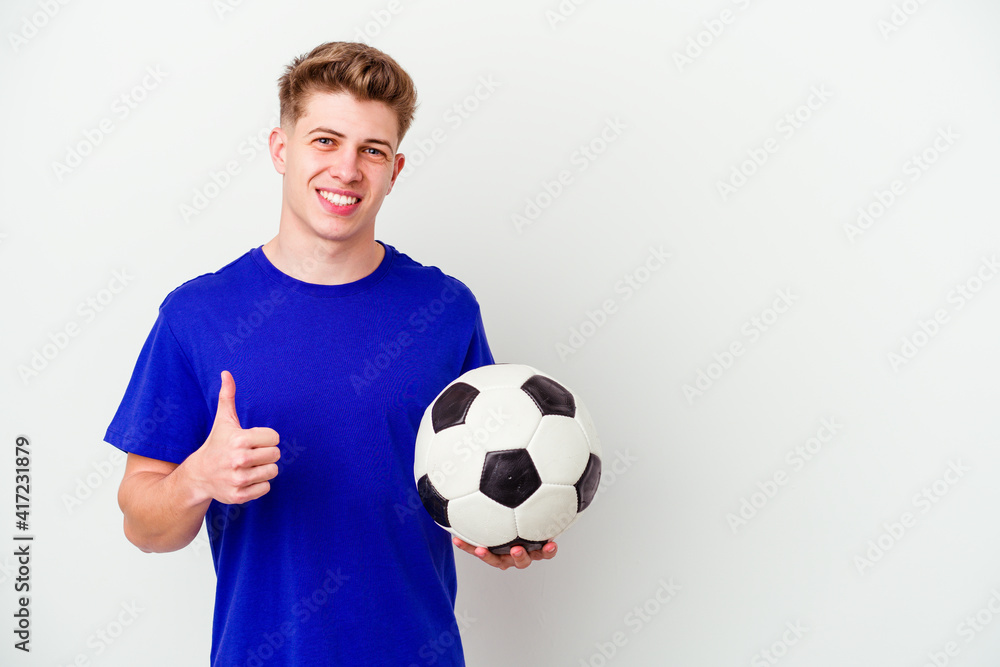 Young caucasian man playing soccer isolated on background smiling and raising thumb up