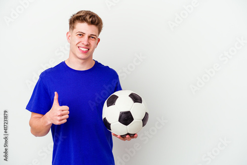 Young caucasian man playing soccer isolated on background smiling and raising thumb up