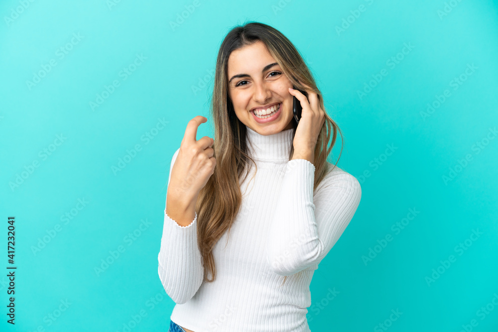 Young caucasian woman using mobile phone isolated on blue background doing coming gesture Young caucasian woman using mobile phone isolated on blue background doing coming gesture