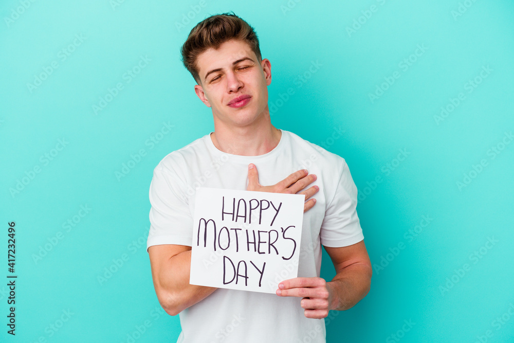 Young caucasian man holding a Happy Mothers day placard isolated on blue background Young caucasian man holding a Happy Mothers day placard isolated on blue background