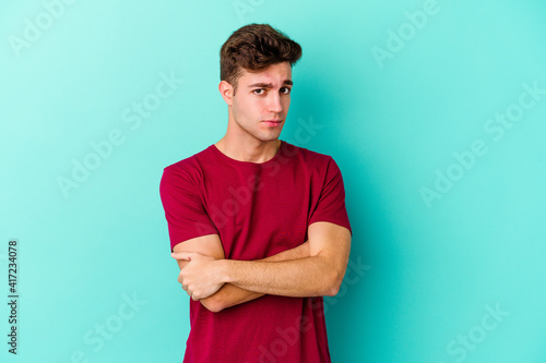 Young caucasian man isolated on blue background suspicious, uncertain, examining you.