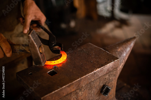 Fotografering The blacksmith forging the molten metal on anvil in smithy